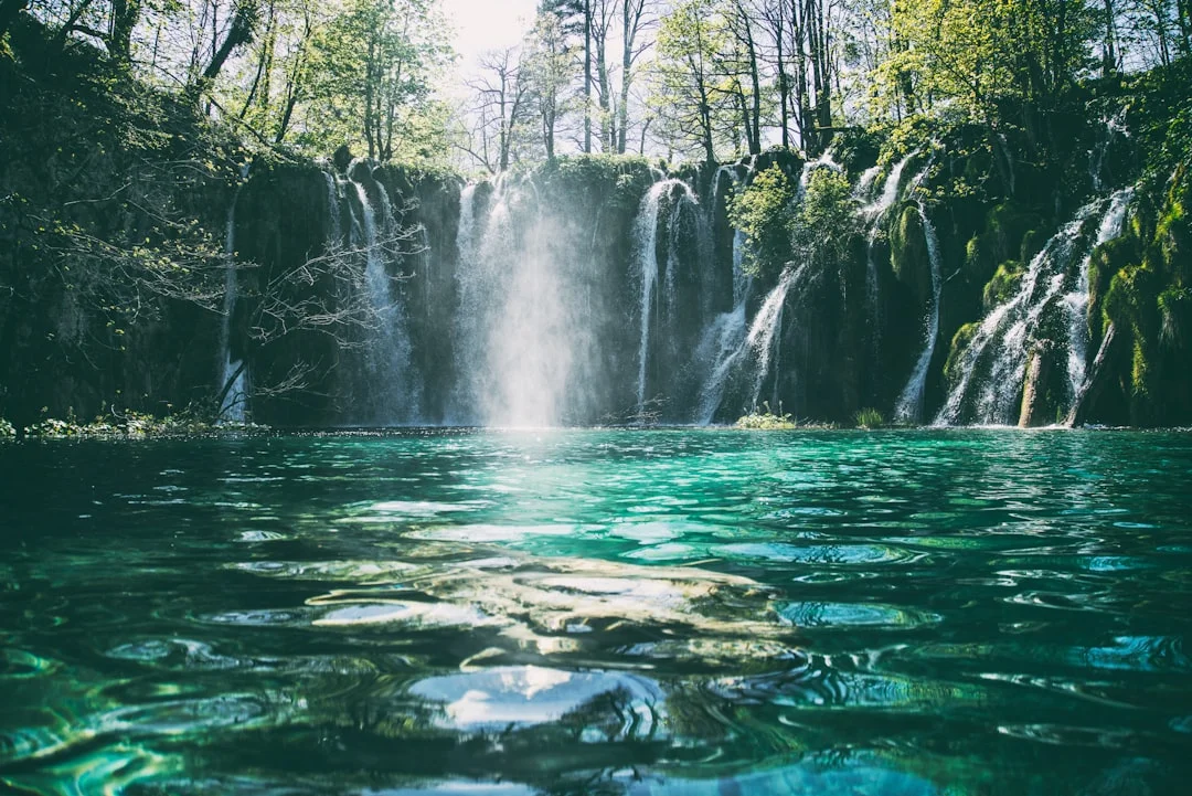 Una hermosa cascada de múltiples niveles que cae en un lago turquesa rodeado de un exuberante bosque verde.